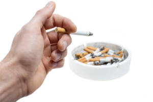 ashtray with cigarettes stubs and hand with burning cigaret
